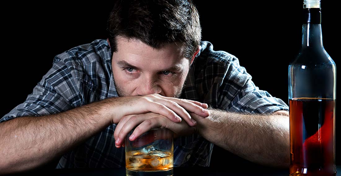 грустный мужчина сидит за столом оперевшись на стакан с алкоголем